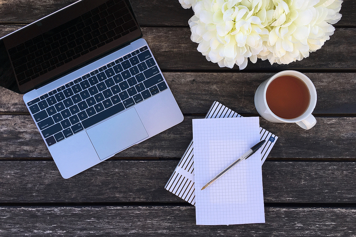 Laptop, cup, paper, and flowers on wooden desk