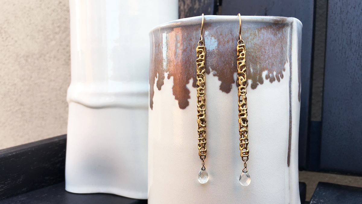 Gold earrings hanging off white cup
