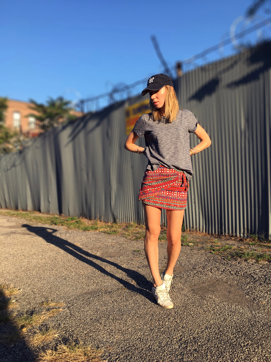Woman posing on street wearing mini skirt with grey tee and Yankees cap