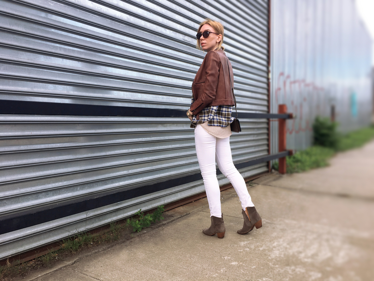 woman posing sideways wearing white jeans and brown leather jacket