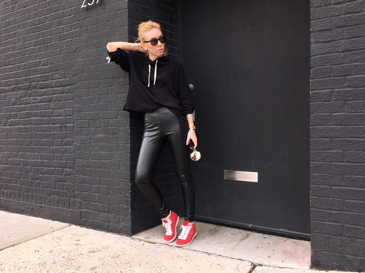 Woman posing wearing all black outfit with red sneakers
