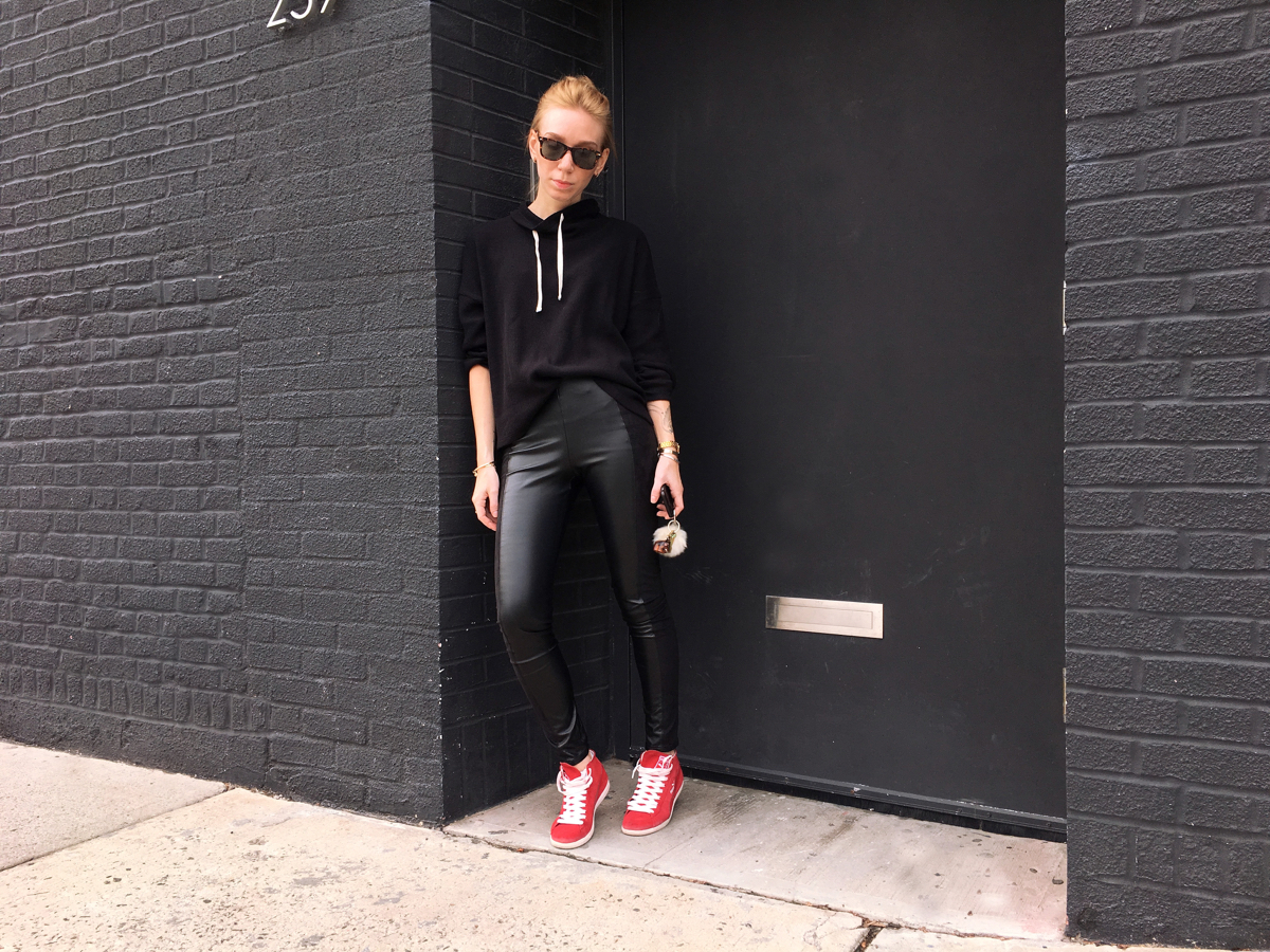 Woman standing wearing all black outfit with red sneakers