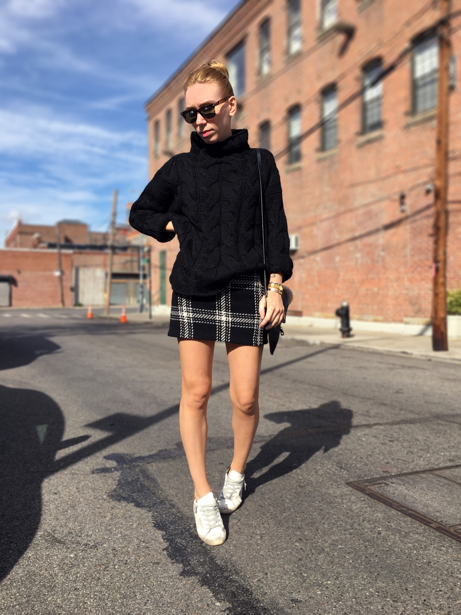 Woman posing in street wearing black turtleneck and a plaid miniskirt