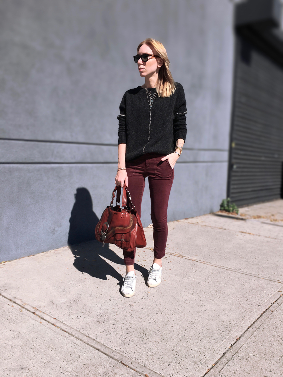 Woman wearing burgundy pants with grey sweater holding a bag