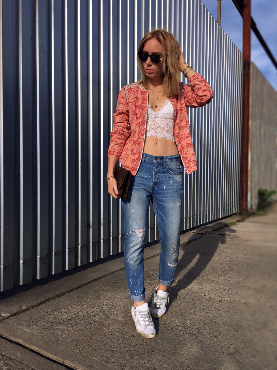 Woman posing wearing pink bomber jacket and white lace top with jeans