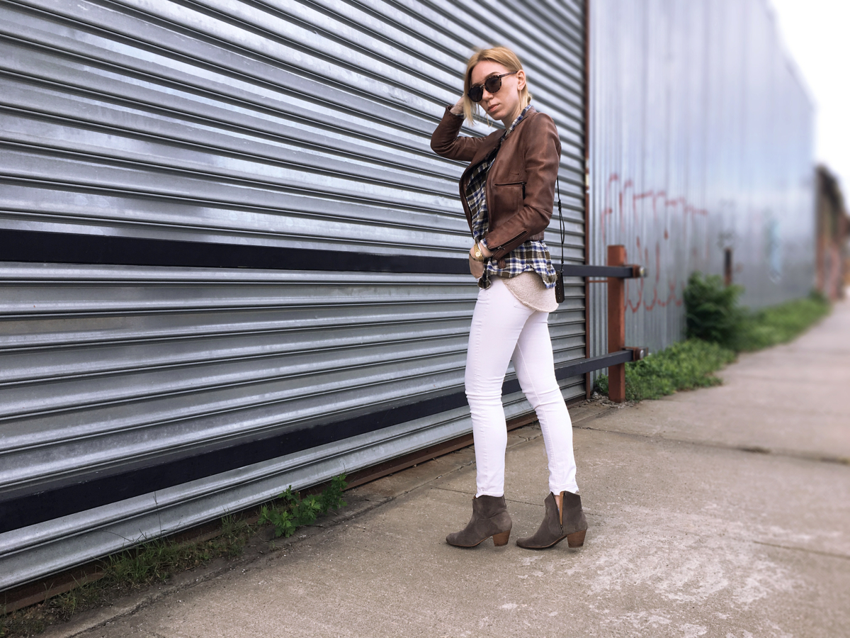 Woman posing sdeways wearing white jeans and brown leather jacket with booties