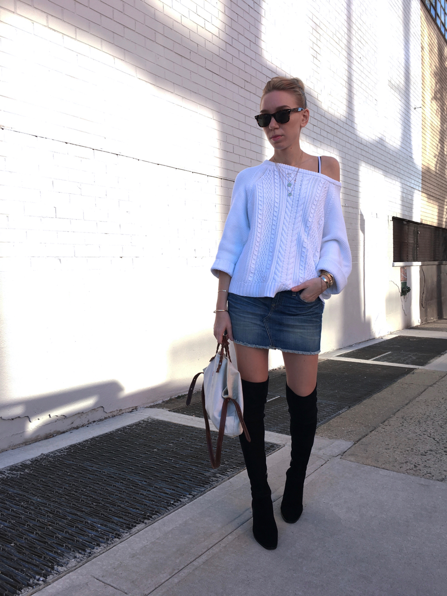 Woman wearing oversized sweater and denim skirt holding bag