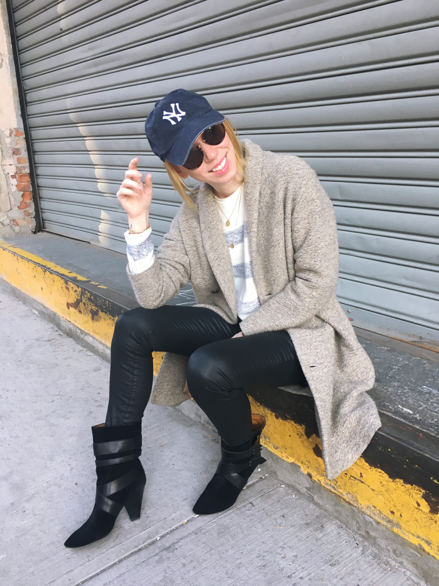 Woman sitting wearing beige coat with striped sweater and black jeans