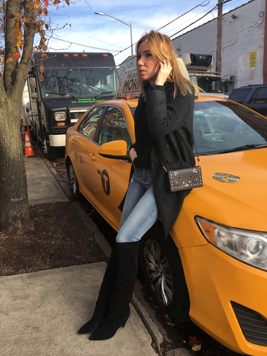 Woman sitting on yellow cab wearing black over the knee boots and outfit