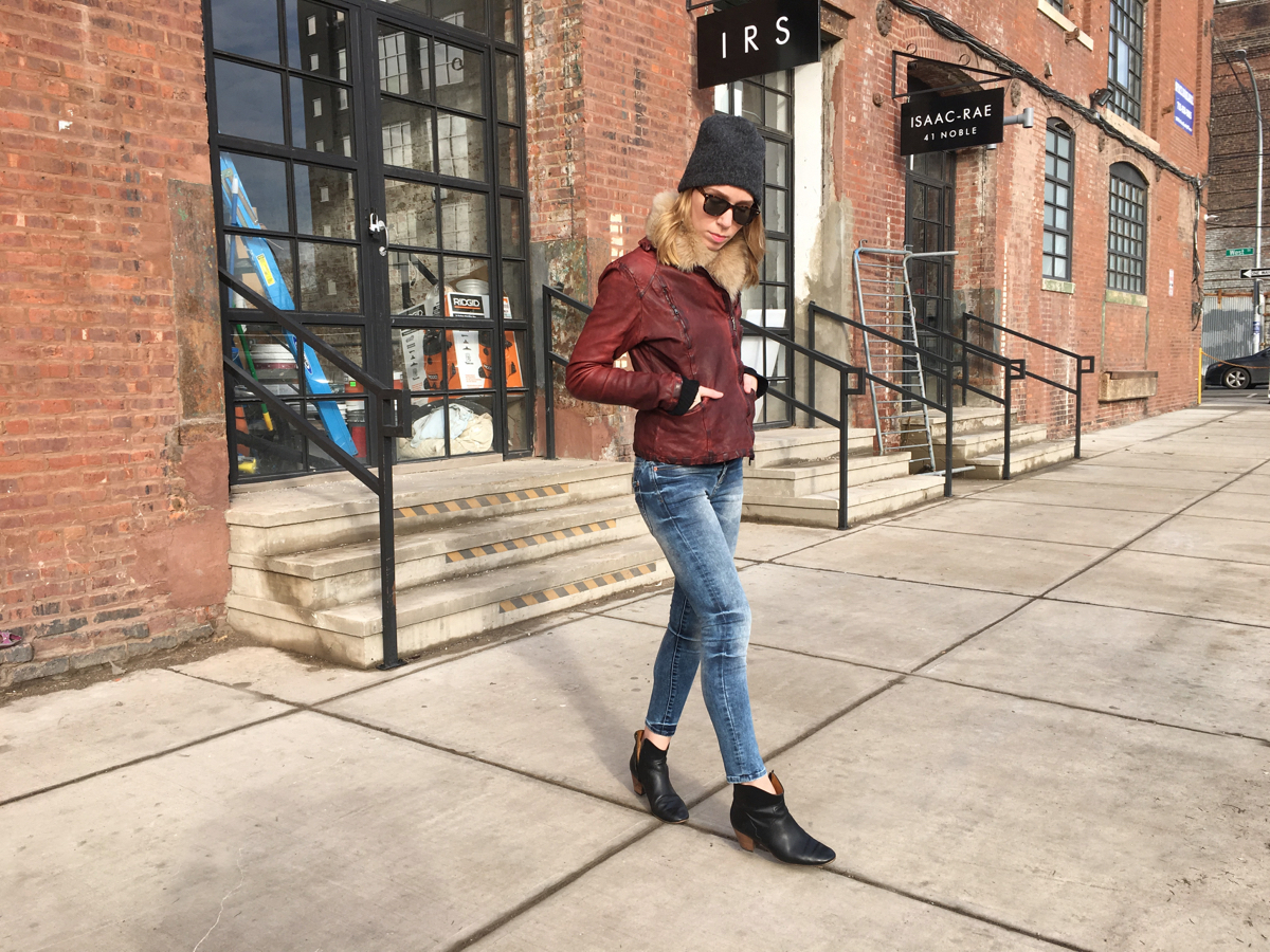 Woman posing sideways wearing blue jeans and red leather jacket