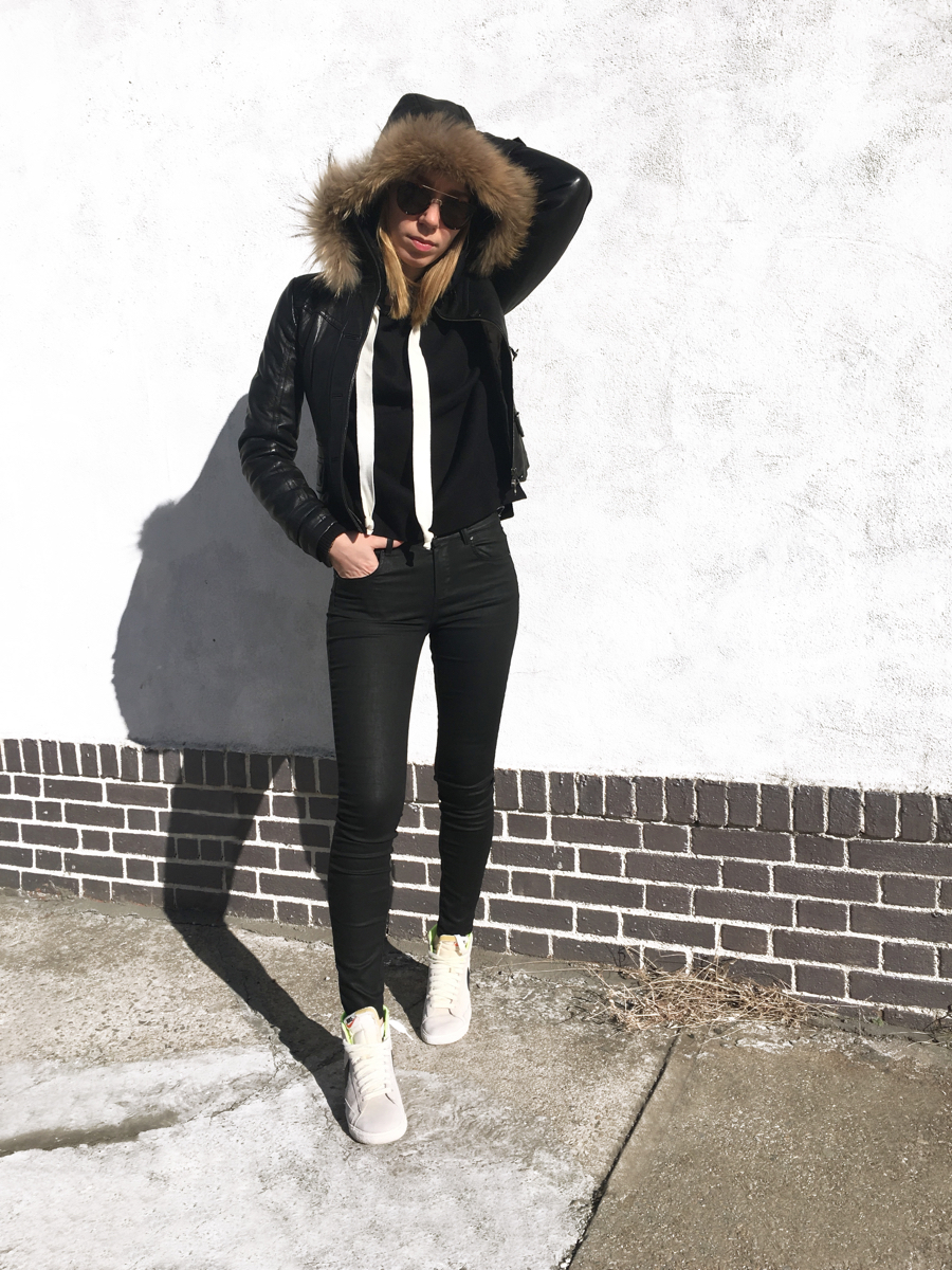 Woman posing in black outfit against white wall