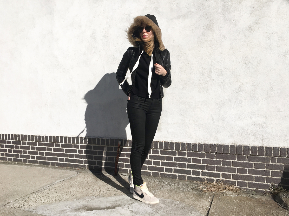 Woman posing in black outfit against white wall