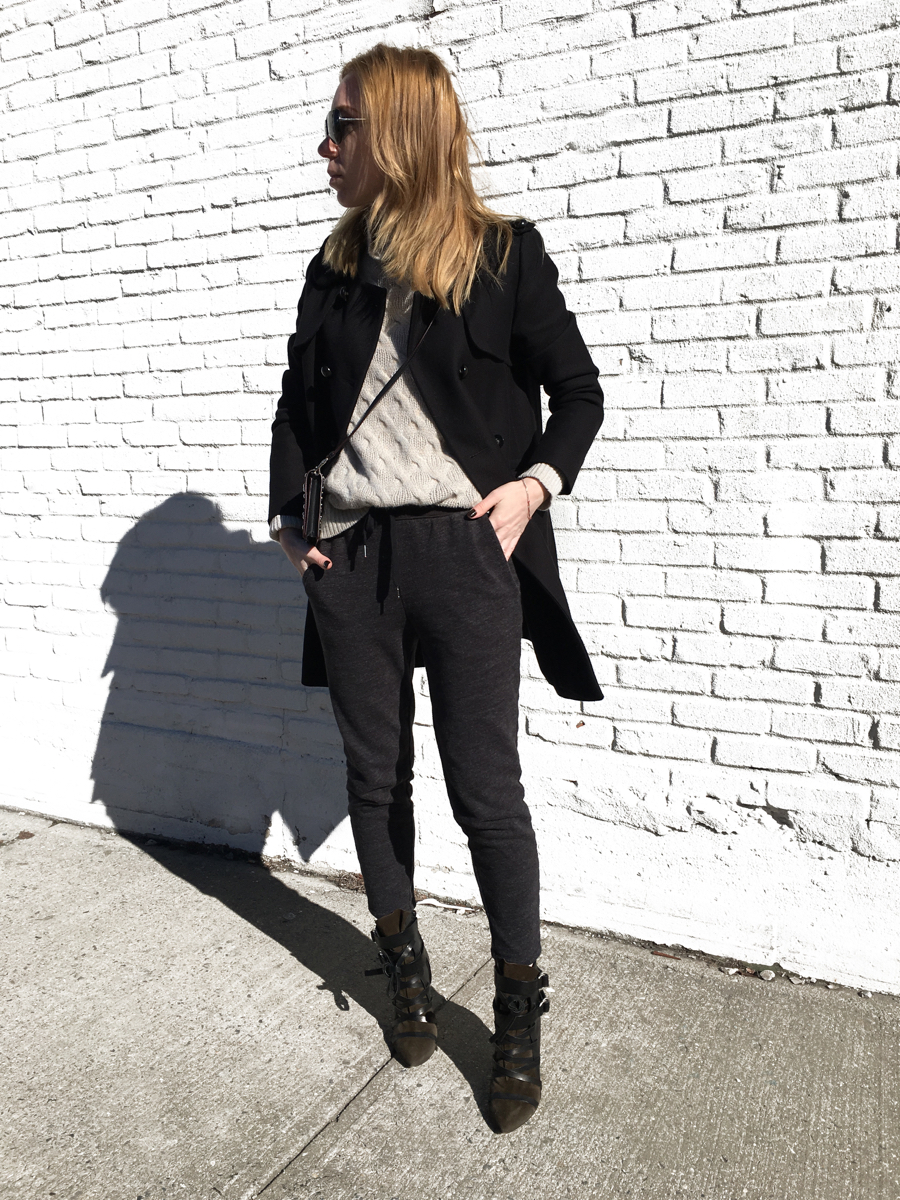 Woman posing in outfit against white brick wall wearing sweats and heels
