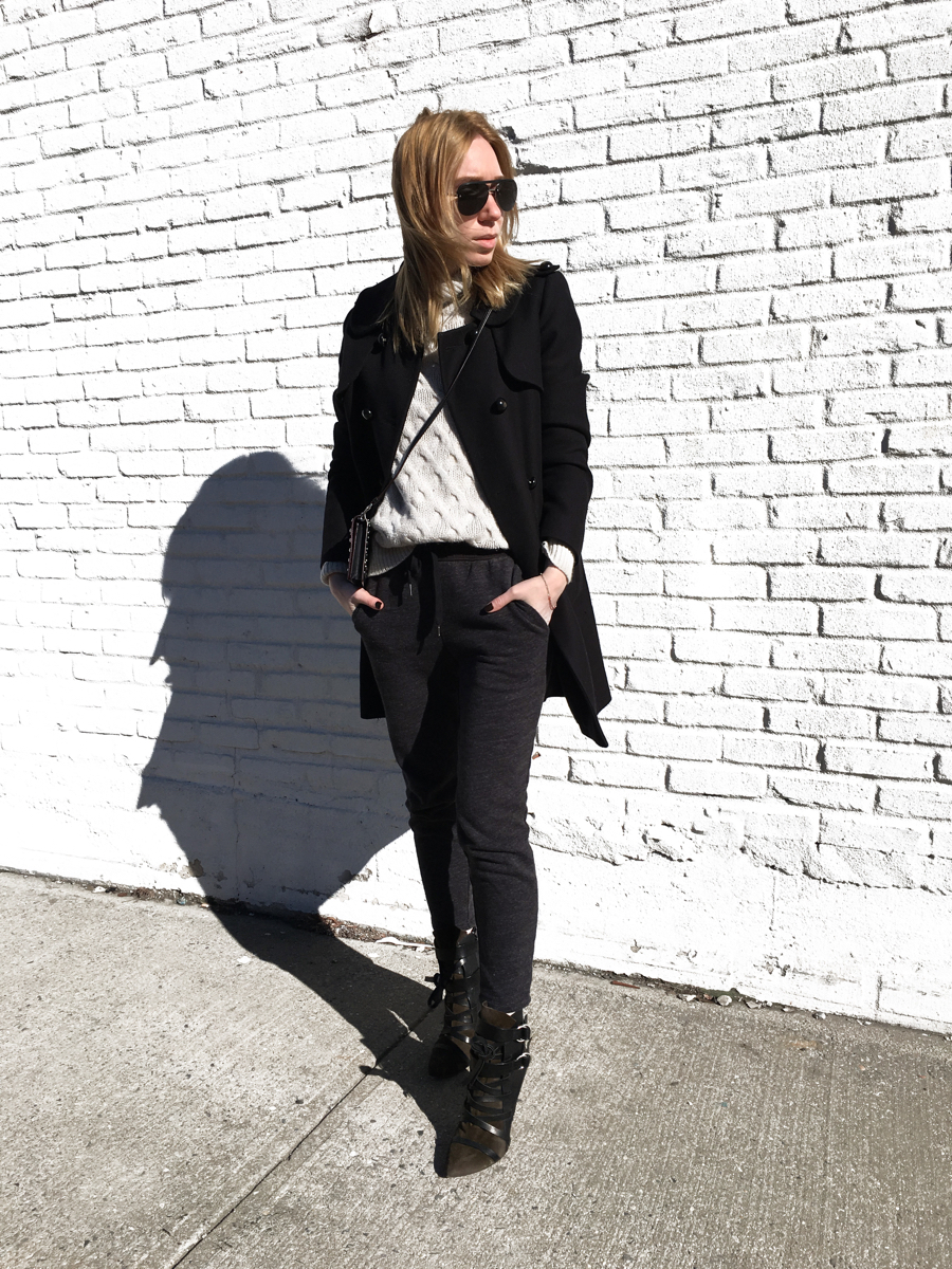 Woman posing wearing black coat with sweats and heels