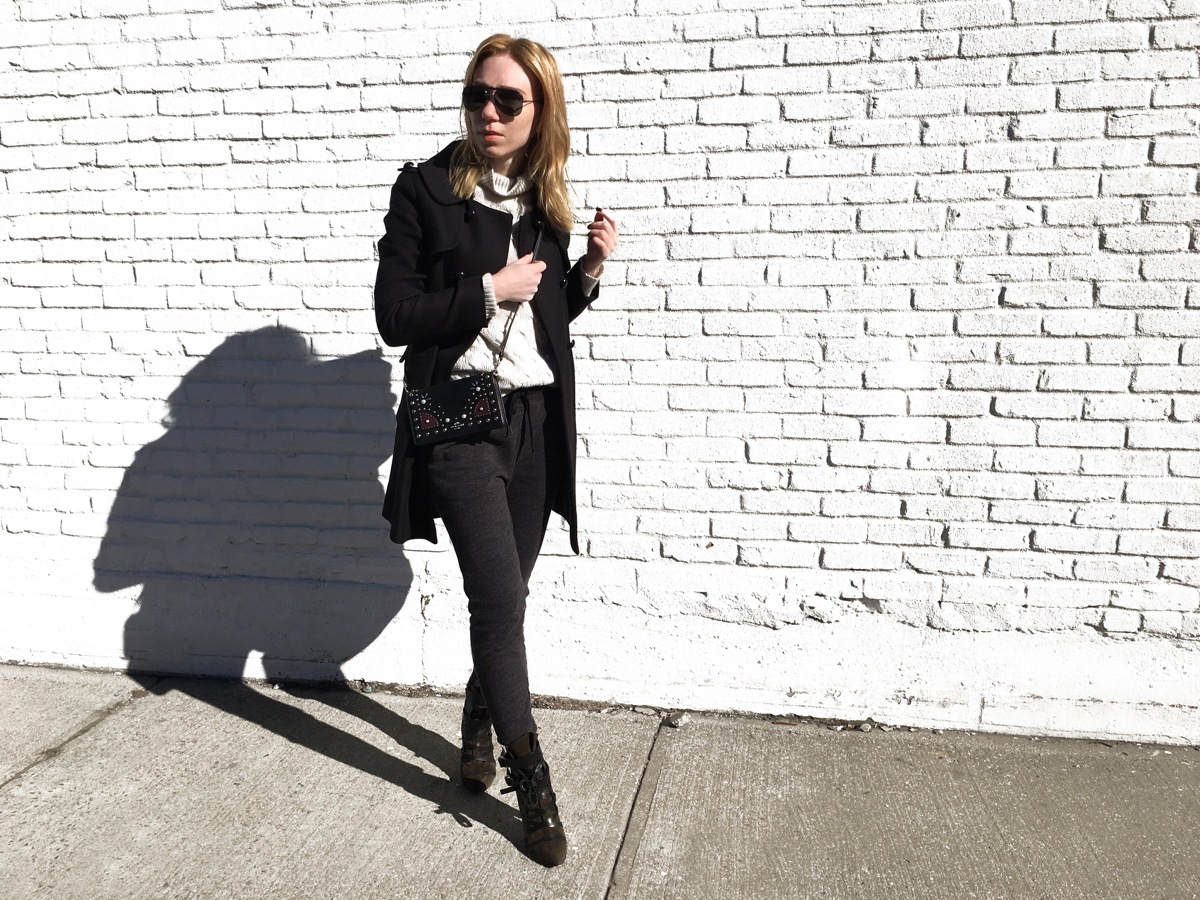 Woman posing in sweats and a coat against white wall