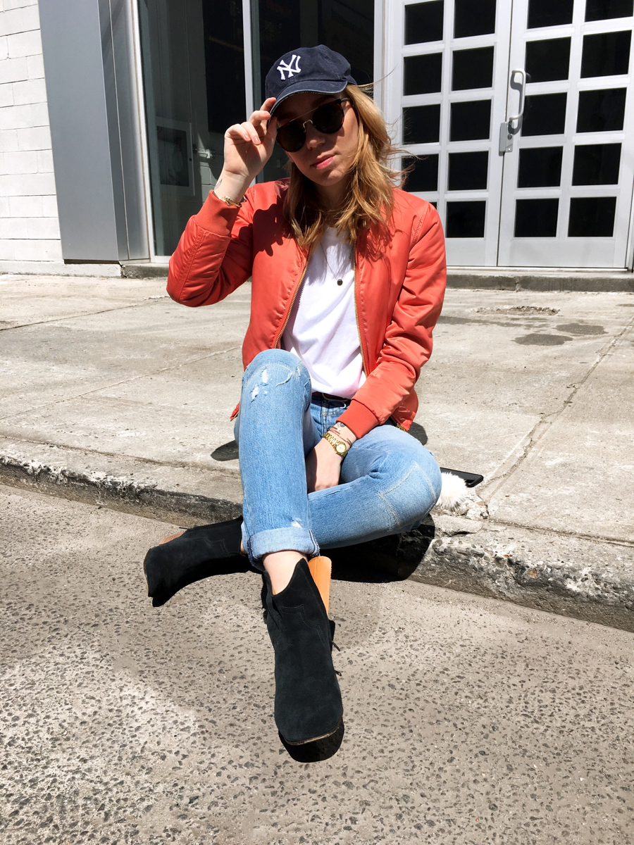 Woman sitting on sidewalk holding on to Yankees cap